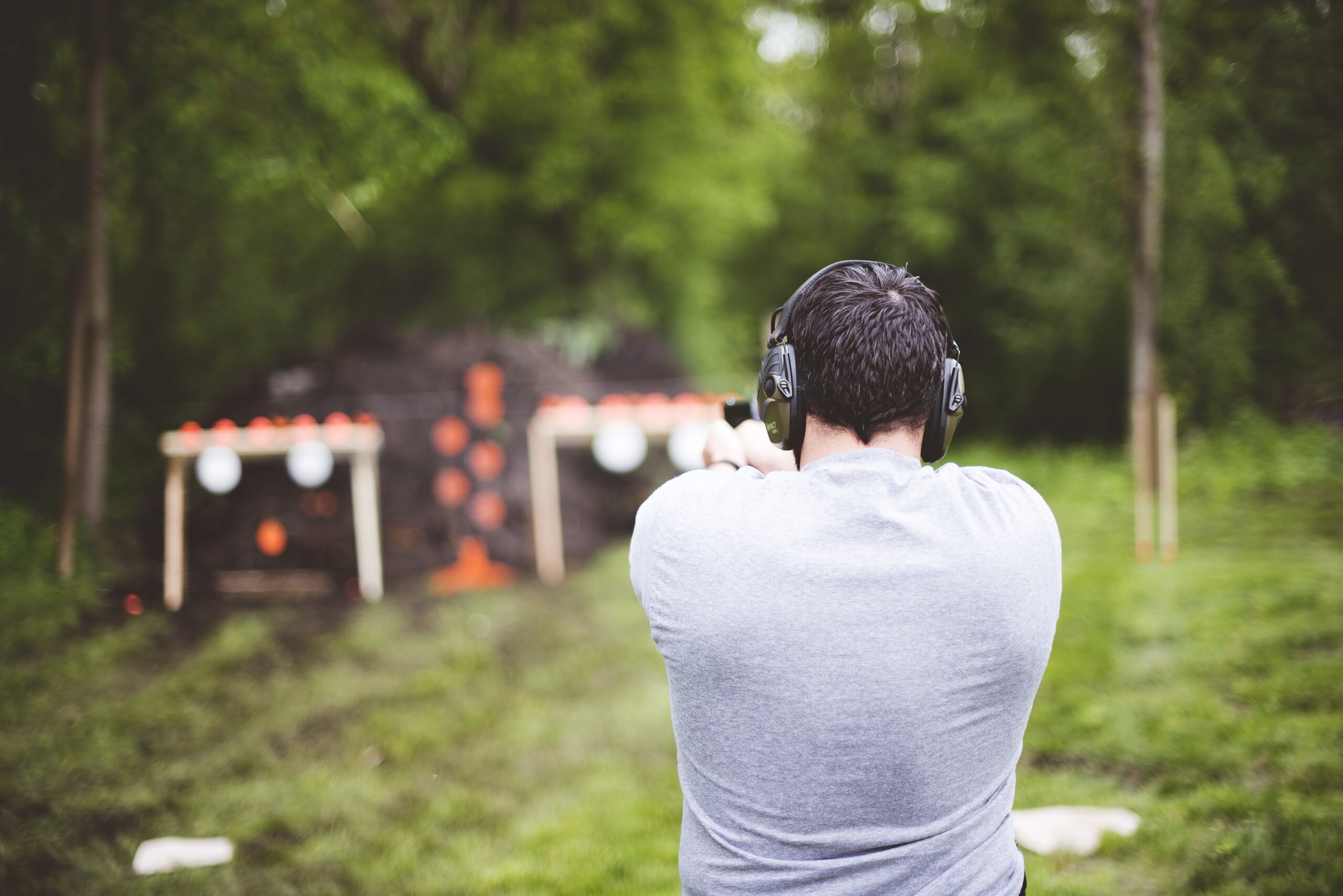 A shallow focus shot from behind of a male shooting a gun at a gun range
